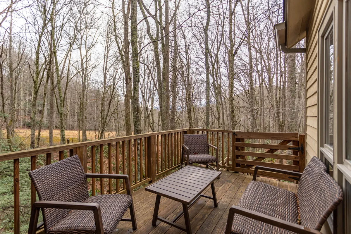 A spacious wooden deck surrounded by lush trees, furnished with comfortable wicker chairs and a table. The setting is tranquil, inviting guests to sit together, relax, socialize, or simply enjoy the sights and sounds of nature. The expansive deck offers ample space for group gatherings, and its integration with the surrounding natural environment highlights the inn's scenic creekside views.
