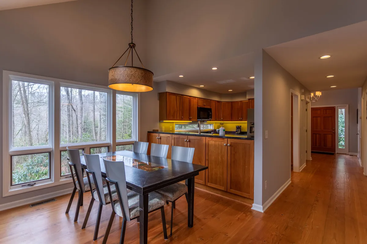 This image features a bright dining space with a sturdy wooden table, modern kitchen cabinetry, and large windows that welcome in natural light. The setting is inviting for a gourmet breakfast or evening cocktails, with hints of the outdoors through the windows.