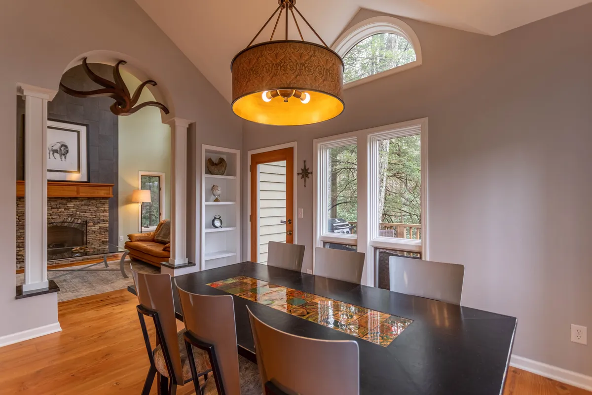 A bright dining area showcasing a large table set for family dinners, a stylish chandelier, expansive windows framing seasonal outdoor views, antler decor, and a fireplace, blending comfort with sophistication.