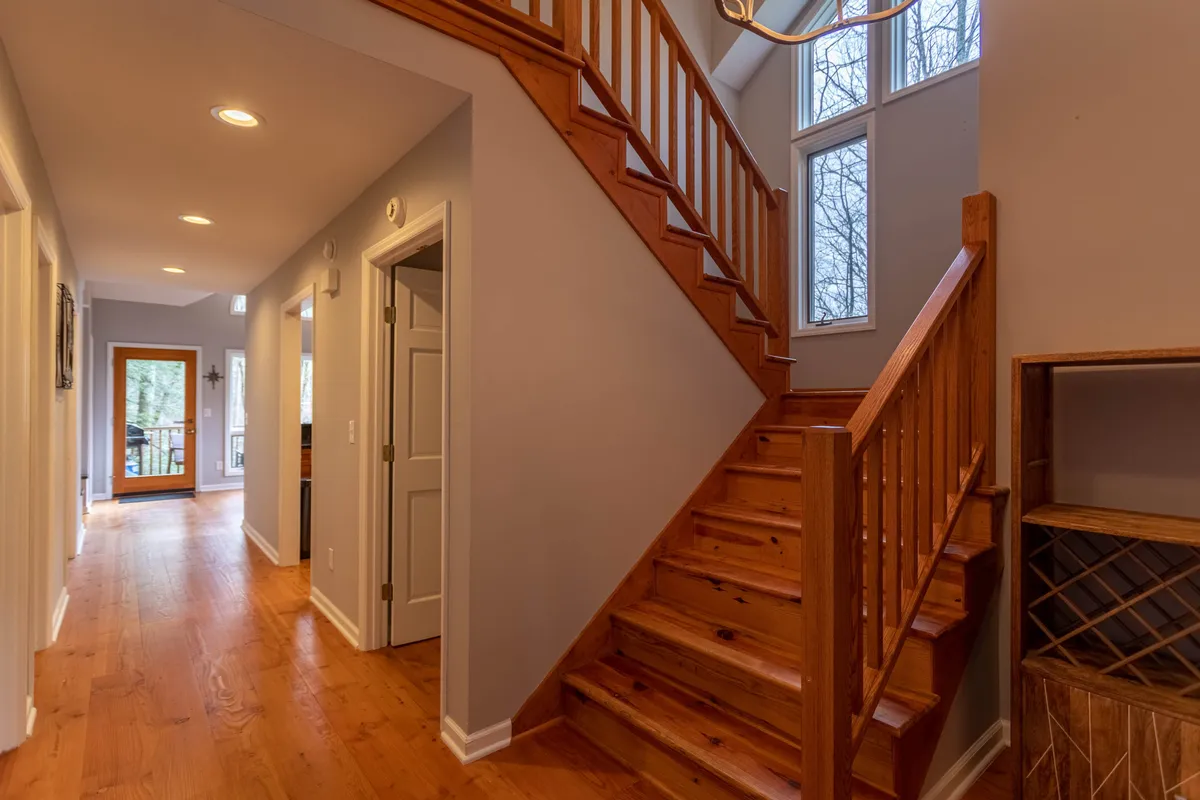 This image features a staircase with large windows that let in ample natural light and a front door, creating a welcoming, transitional space between indoors and outdoors. The space is inviting, suggesting movement from the cozy interior to the natural world outside, echoing the section’s mention of a hidden staircase leading down to a creek.
