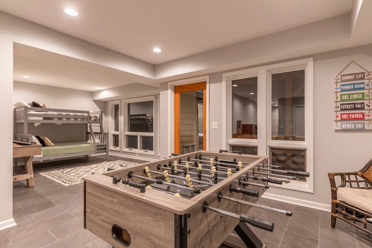 A playful bunk area with a foosball table, bunk beds, large windows, and a decorative sign. The space feels fun and welcoming, perfect for teens or children to unwind and play.