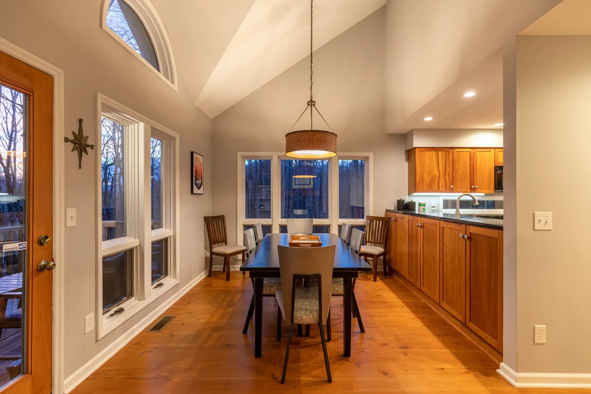 The dining table sits adjacent to large windows, with a hanging light fixture overhead and cabinets visible in the background. The arrangement suggests easy flow from kitchen to dining area, perfect for enjoying meals together while taking in sunset views.