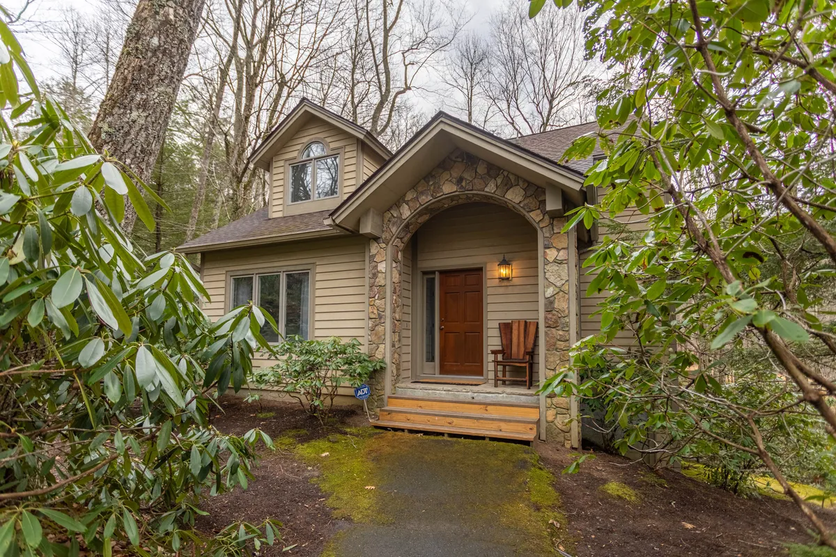 The inviting front porch of Crooked Creek Inn features a decorative stone archway, wooden door, and lush greenery. The porch offers cozy seating, perfect for sipping coffee or reading a book while taking in the mountain air. The scene creates a welcoming first impression and underscores access to outdoor relaxation spaces.