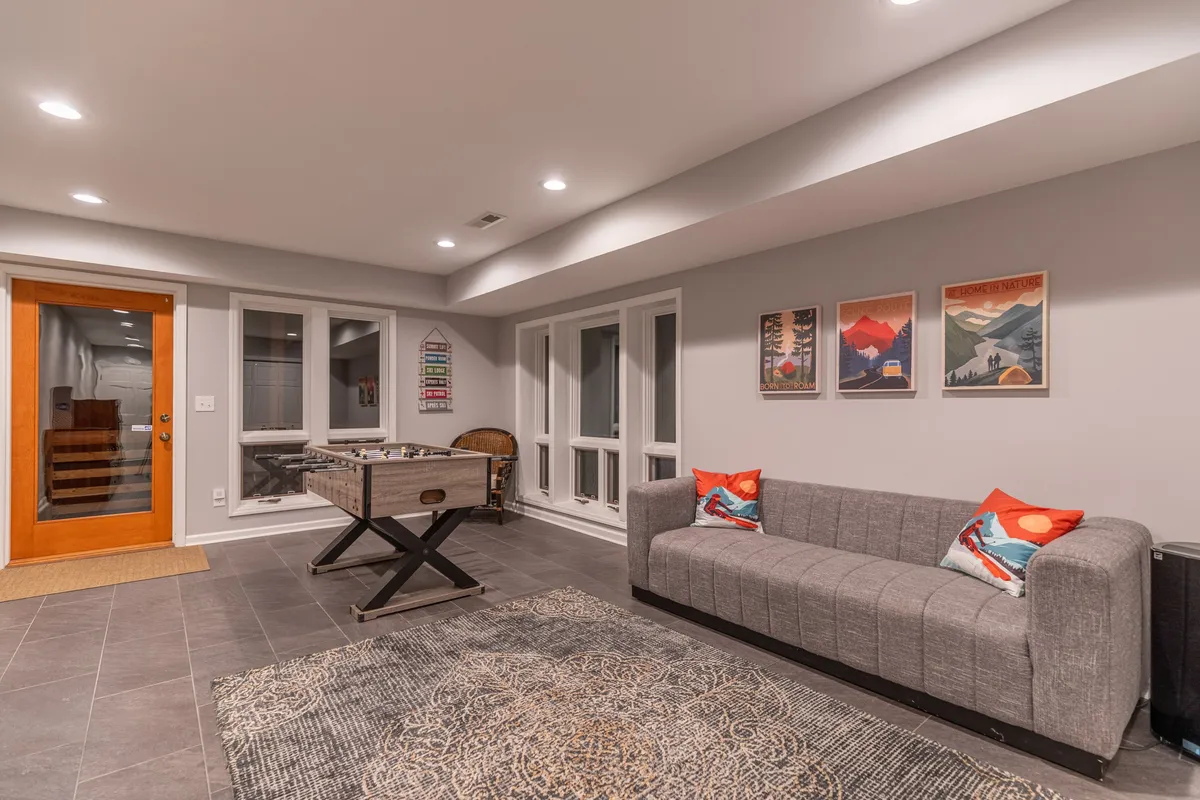 A casual and friendly game room setting with a pool table, comfortable gray couch, colorful artwork, and a wooden door that hints at easy transitions between indoor fun and outdoor exploration. The space is inviting for socializing and winding down after a day of adventure.