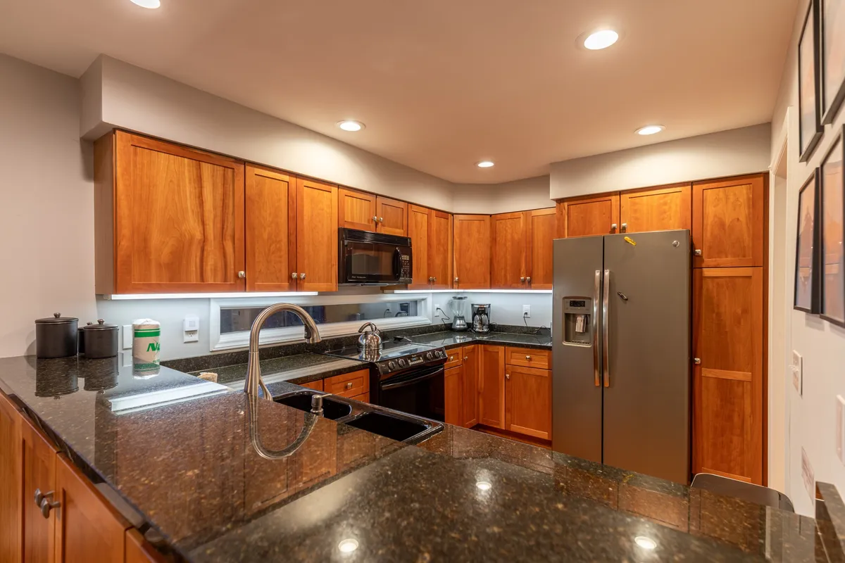 A close-up view of the kitchen area with warm wooden cabinetry, granite countertops, and stainless steel appliances. The setup suggests both functionality and style, with visible cookware and utensils ready for use—details that reinforce the idea of a fully-stocked culinary space.