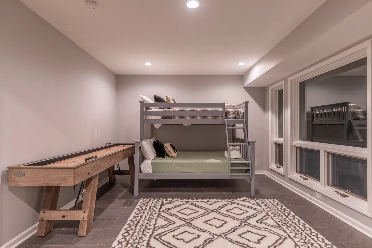 A cozy space with a bunk bed, a shuffleboard table, and large windows allowing for natural light. The arrangement shows both sleeping and entertainment options in a relaxed, family-friendly setting.