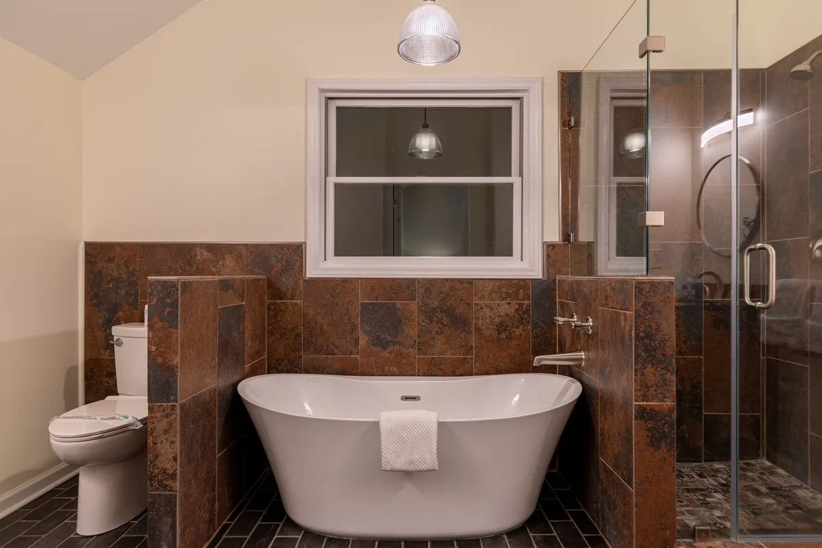 A modern bathroom with a freestanding soaking bathtub, glass shower enclosure, and an elegant tile accent wall. Natural light fills the room, creating a spa-like atmosphere ideal for relaxation and self-care.